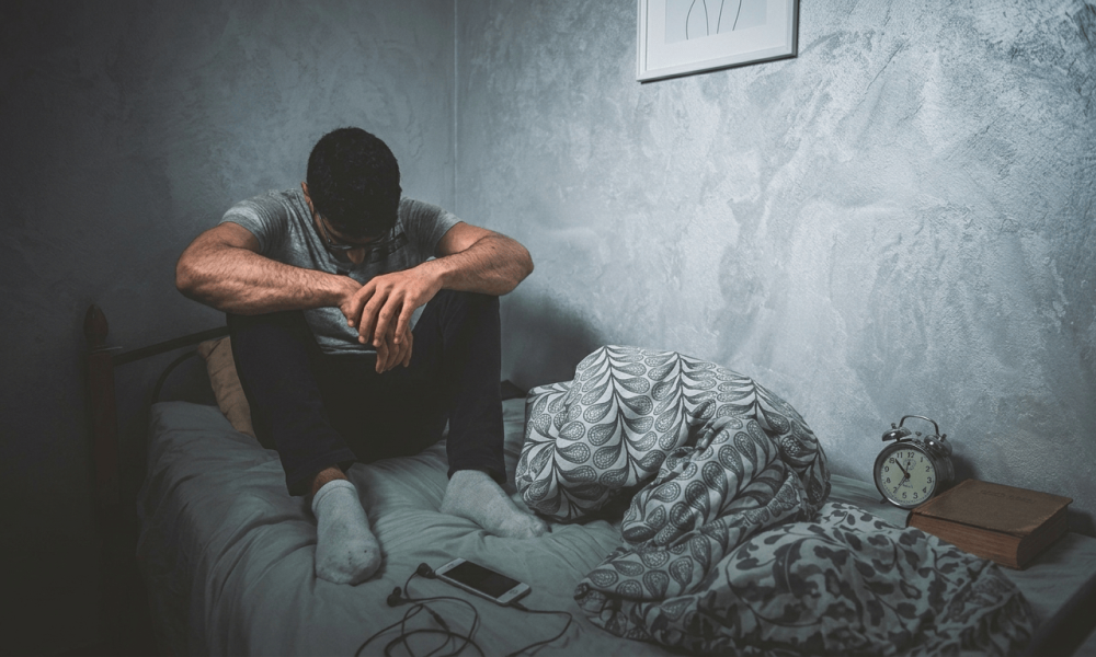 A man sitting on the edge of a bed with his head in his hands next to a phone, illustrating anxious attachment and hyper-vigilance in relationships.